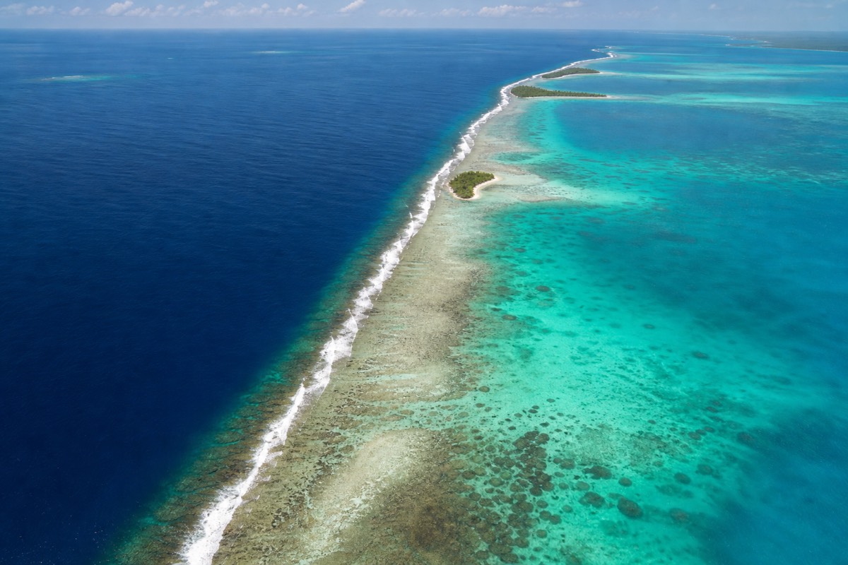 Aerial view of Belize Barrier Reef snorkeling waters, with surf breaking between pale lagoon and deep blue Caribbean sea