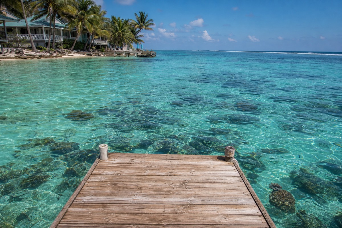 A dock reaching over shallow turquoise water on a Belize caye with the barrier reef breaking in the distance