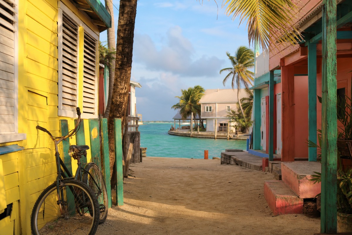 A snorkeling in Caye Caulker boat leaves the sandy waterfront, with shallow turquoise water and wooden docks